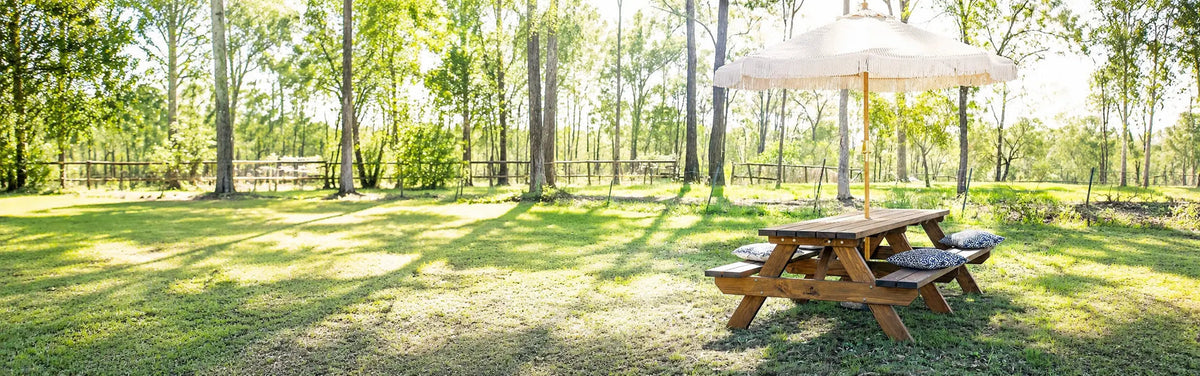 JJ Timber Design picnic table beneath a parasol in a leafy outdoor setting